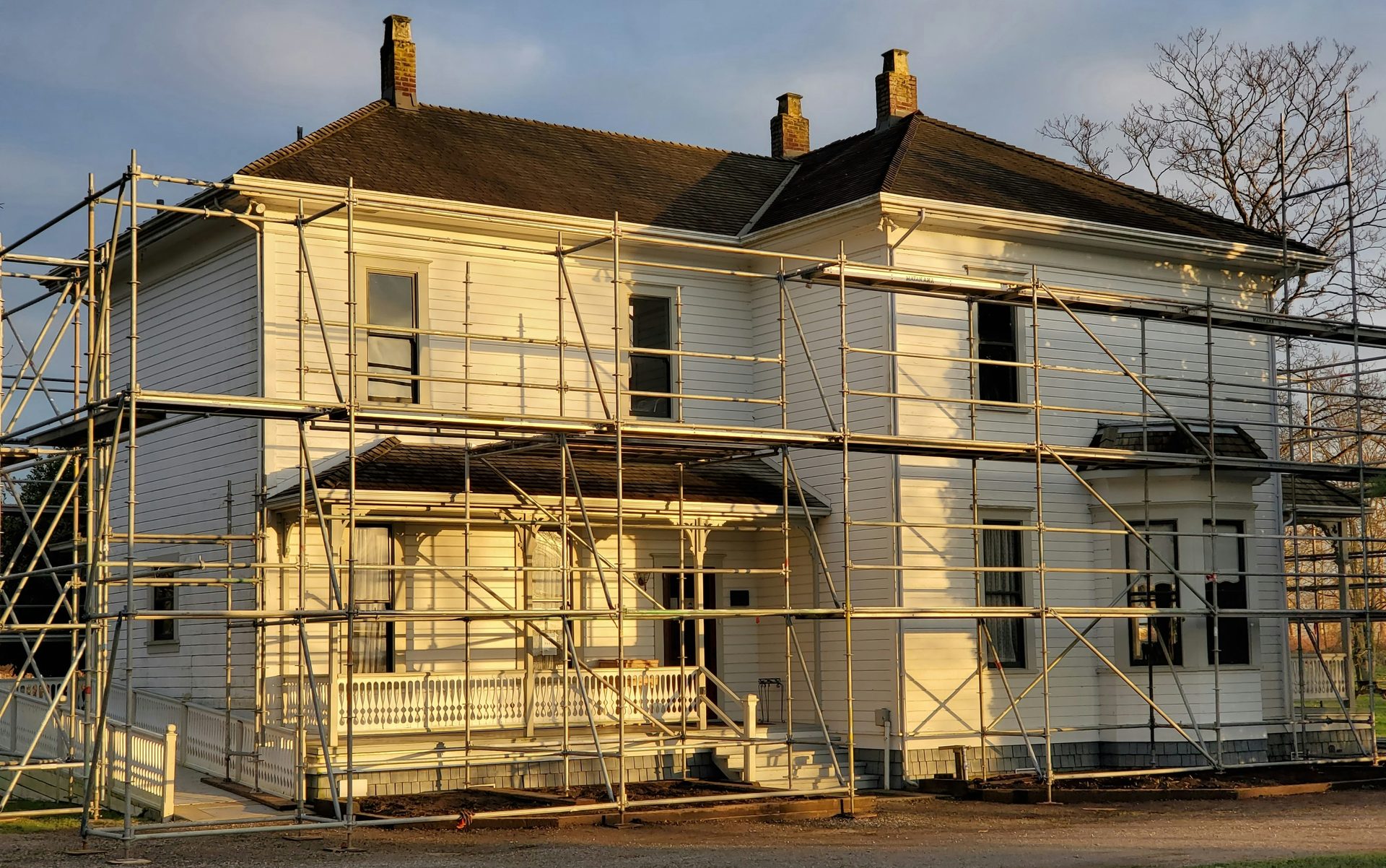 A clapboard house wrapped in scaffolding at golden hour, mid-renovation