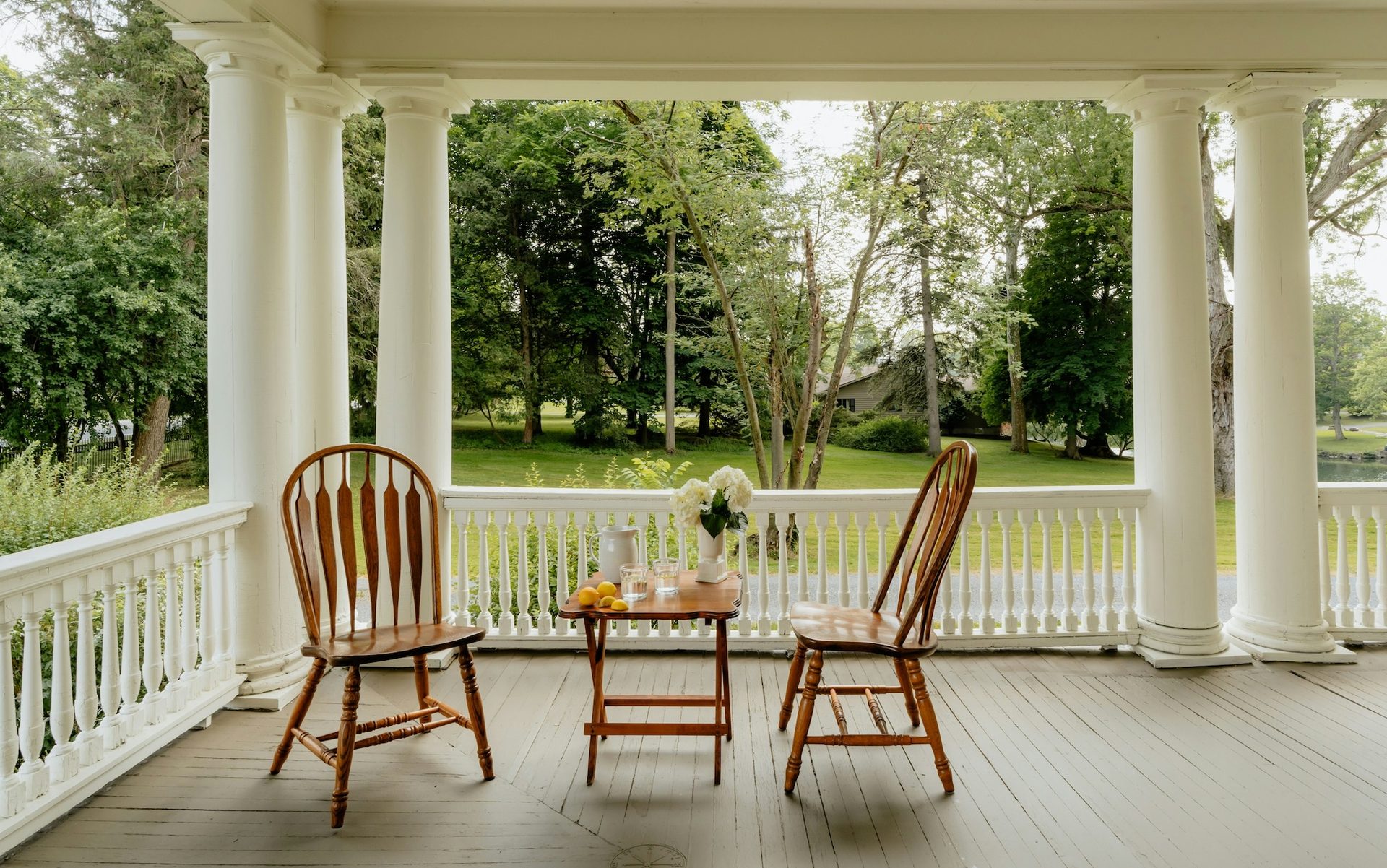 A wide covered porch with wooden chairs looking out over a green lawn