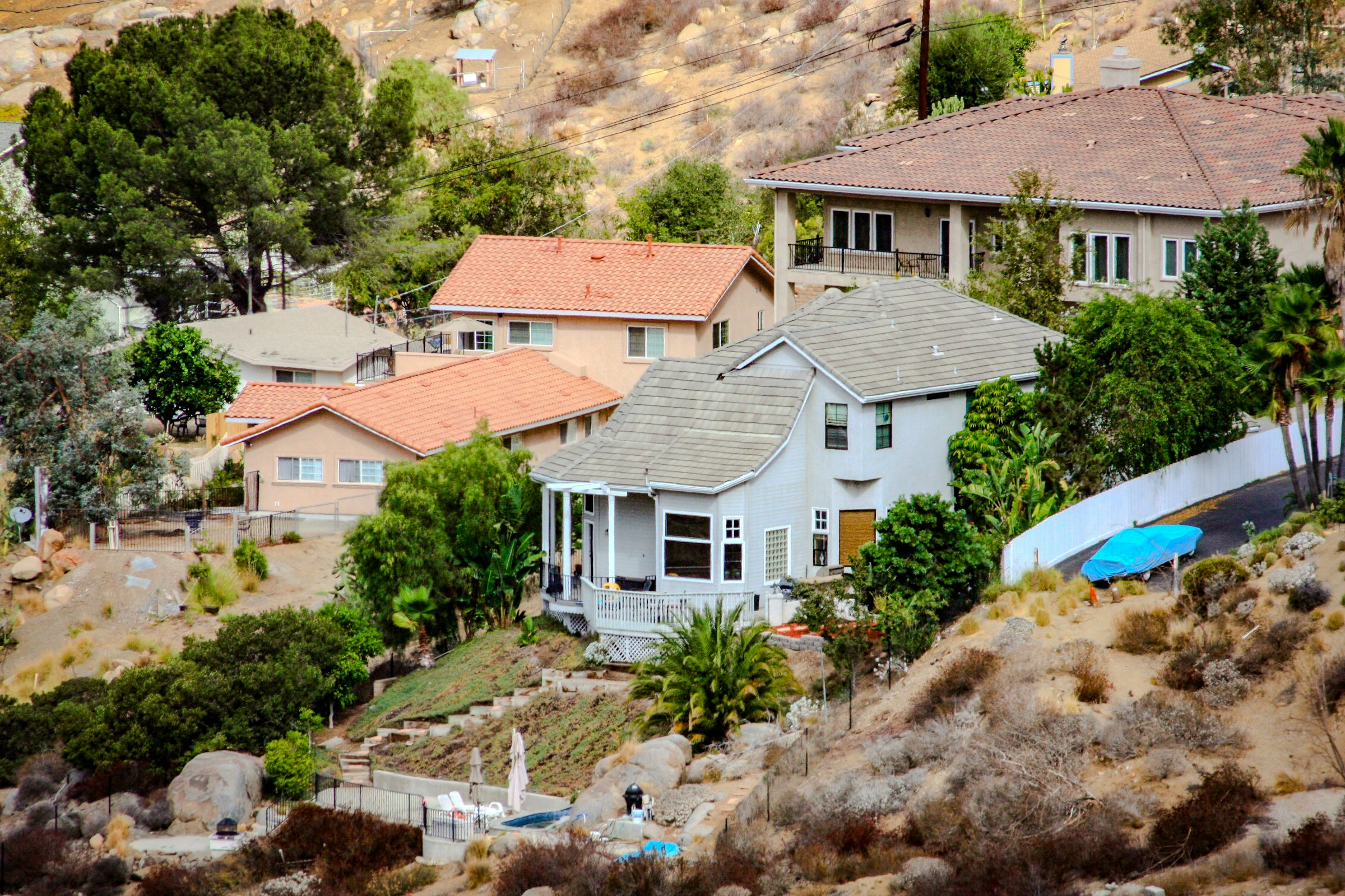 Houses scattered across a sunny, arid California hillside with dry brush between them