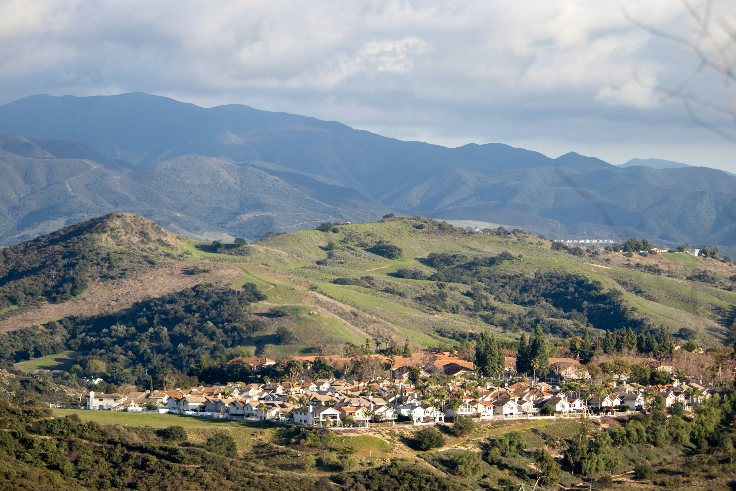 A Southern California subdivision spread across a valley floor, with chaparral-covered hills and mountains rising behind it