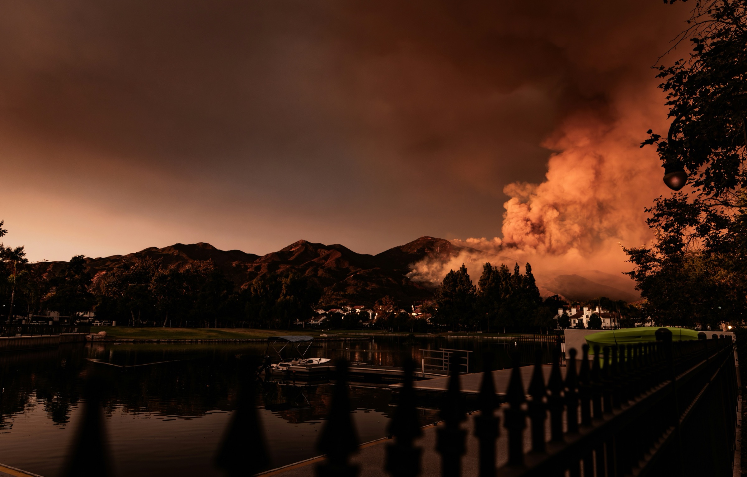 Wildfire smoke rising behind a lakeside California neighborhood at dusk