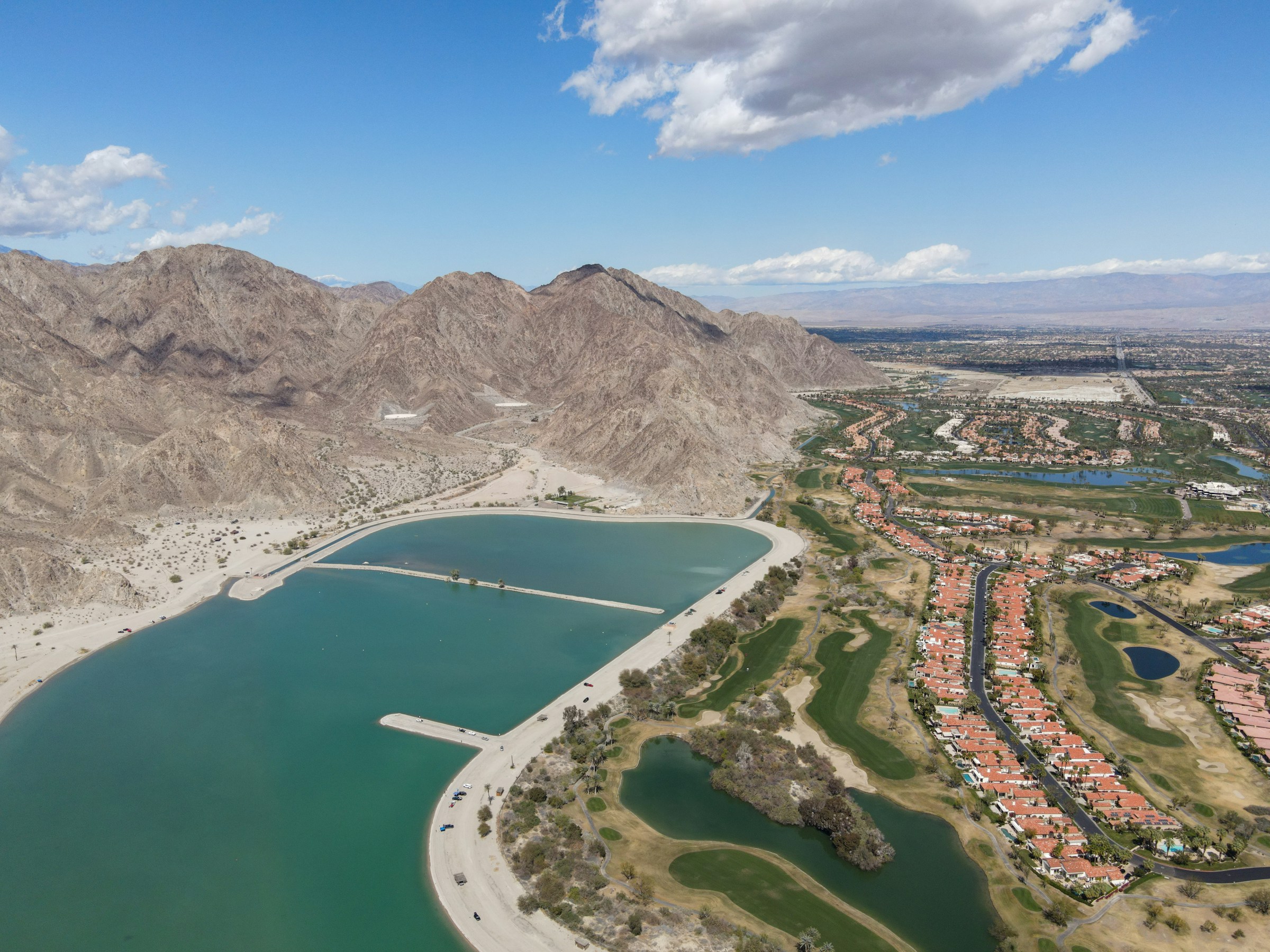 An aerial view of a desert reservoir beside a residential community, with bare mountains beyond